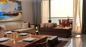 Una sala de estar moderna con un sofá, una mesa de comedor y sillas. Hay un cuadro en la pared y una vista al mar a través de ventanas amplias.