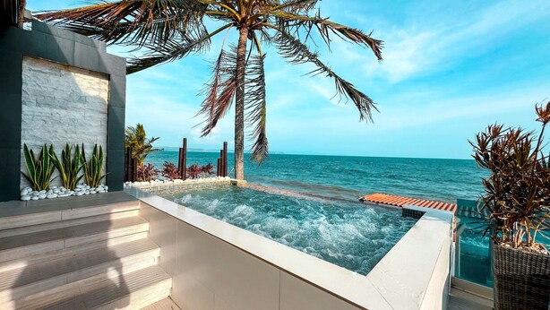 Un área de piscina moderna al aire libre con vista al mar, rodeada de palmeras y plantas.