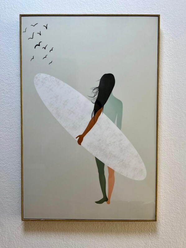 Una obra d'art emmarcada que mostra una persona amb una taula de surf, amb ocells volant al fons.
