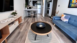 Ein modernes Wohnzimmer mit einem blauen Sofa, einem runden Couchtisch und einem Fernseher an der Wand.