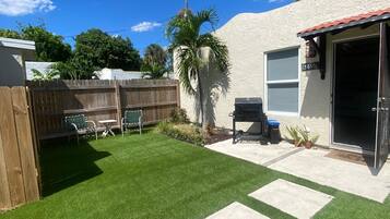 Un jardin avec une pelouse artificielle, une clôture en bois, un palmier et une porte de garage.