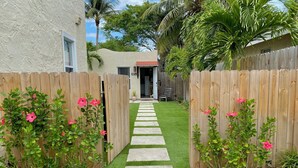 Un camino que lleva a una casa con cerca de madera, césped verde y plantas de flores rosadas.