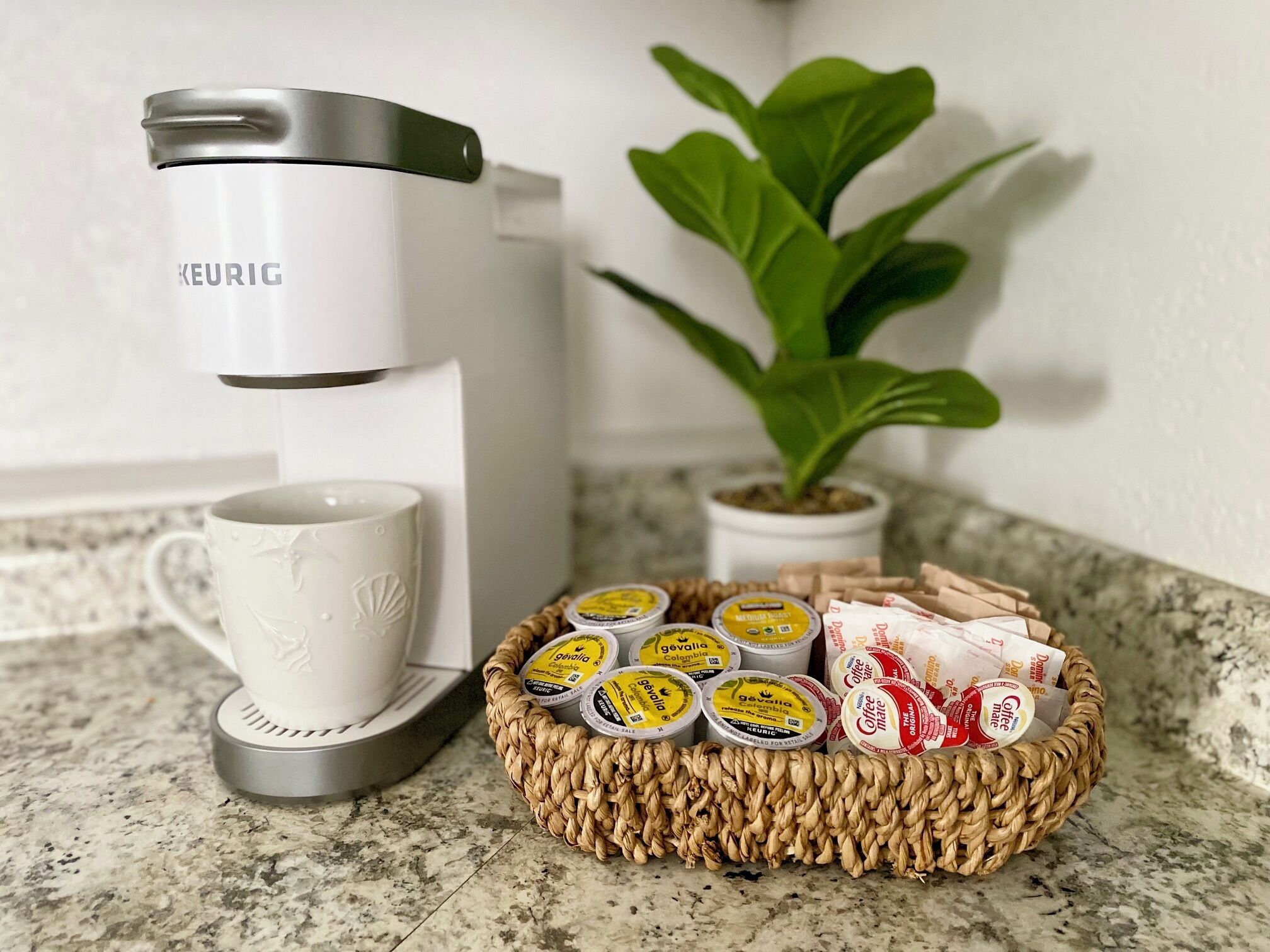 Une machine à café Keurig, une tasse blanche et un panier de dosettes de café sur un comptoir de cuisine.