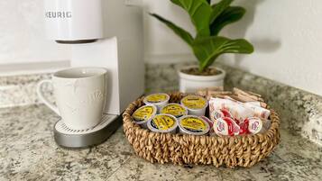 Une machine à café Keurig, une tasse blanche et un panier de dosettes de café sur un comptoir de cuisine.