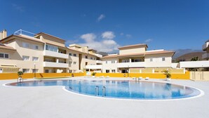 A swimming pool surrounded by multi-story buildings with balconies, a clear sky, and a mountainous background. - Home2Book Design Duplex Puertito de Güímar, Pool (Puertito de Güímar)