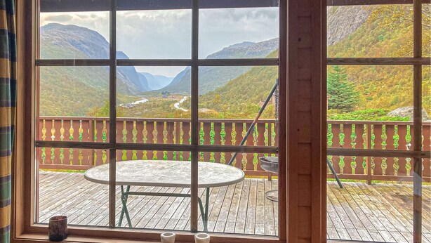 A wooden deck with a table and chairs, overlooking a mountainous landscape with a winding road. - Gorgeous home in Dirdal (Dirdal)