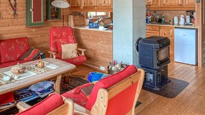 A cozy cabin interior with a wooden dining table, a red upholstered chair, a television, and a small refrigerator. - Gorgeous home in Dirdal (Dirdal)