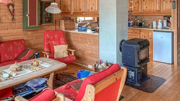 A cozy cabin interior with a wooden dining table, a red upholstered chair, a television, and a small refrigerator.