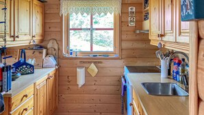 A wooden cabin kitchen with a window, wooden cabinets, a sink, and various kitchen utensils. - Gorgeous home in Dirdal (Dirdal)
