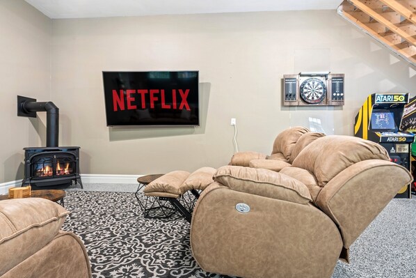 Una sala de estar con un letrero de Netflix, una chimenea, un dardo y una consola Atari 50.