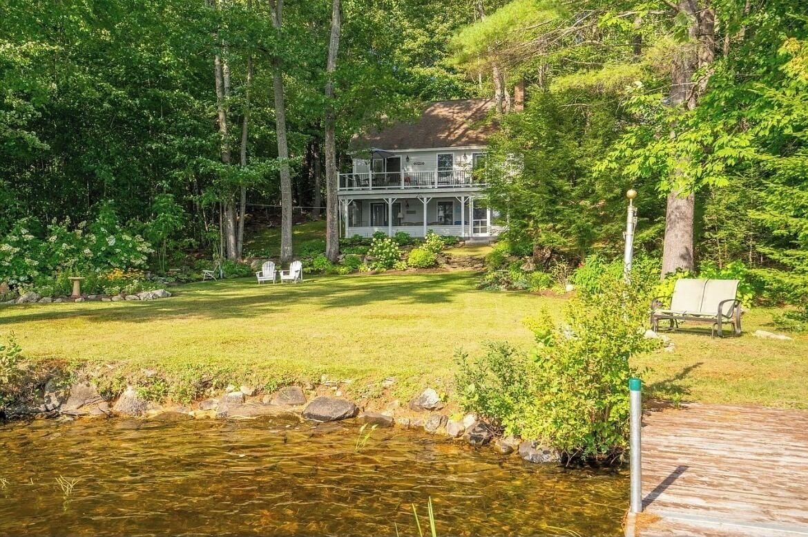 A two-story house with a porch, surrounded by a well-maintained lawn and a small pond.