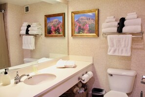 Une salle de bain avec un lavabo, des toilettes et des porte-serviettes. Deux tableaux encadrés ornent le mur, et un miroir est placé au-dessus du lavabo.