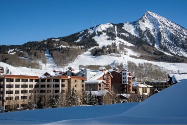 Un hôtel à plusieurs étages, avec des pistes de ski en arrière-plan et une montagne.