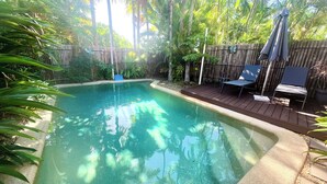 A rectangular swimming pool with clear water, surrounded by a wooden deck and a bamboo fence.