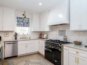 A kitchen with white cabinets, a black stove, and a patterned window treatment.