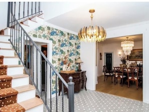 Una escalera con un muro decorado, una araña y un comedor con sillas y una mesa.