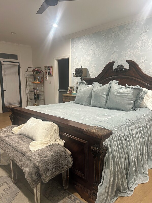 Een slaapkamer met een groot bed, een houten hoofdbord, een bankje, een wandplank en een deur.