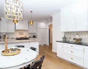 Una cocina con muebles blancos, una mesa redonda para comer e iluminación colgante.