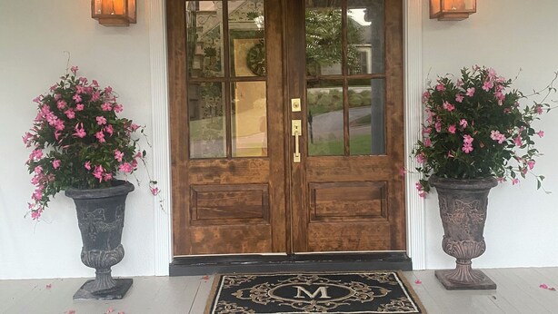 A wooden double door with glass panels, flanked by two potted plants with pink flowers, and a doormat with a monogram. - Welcome to the perfect Oxford getaway for an Ole Miss game.  (Oxford)