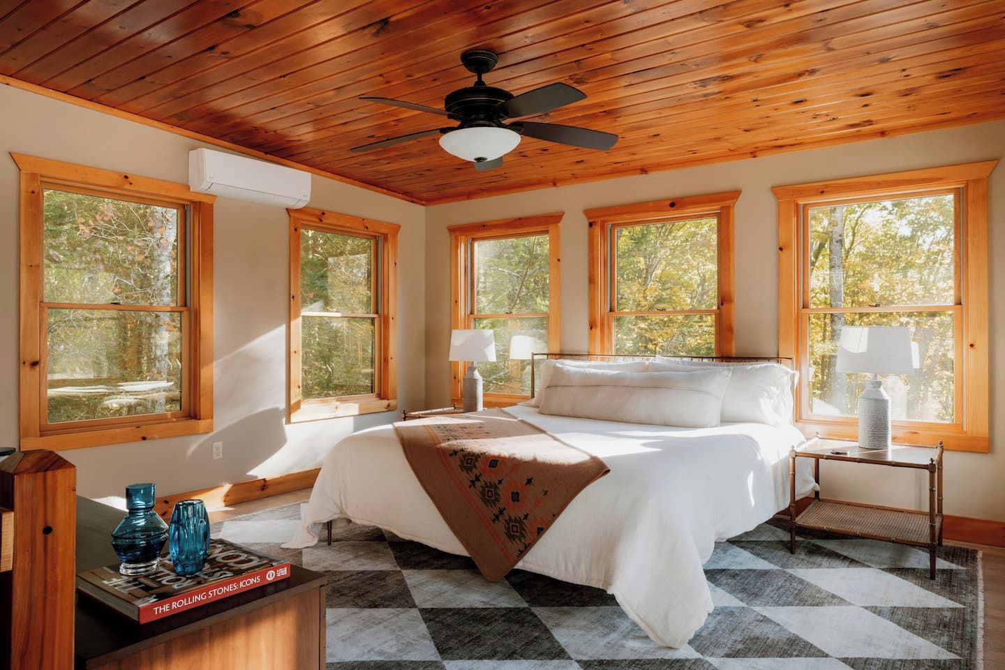 A bedroom with a bed, two bedside tables, a ceiling fan, and large windows.