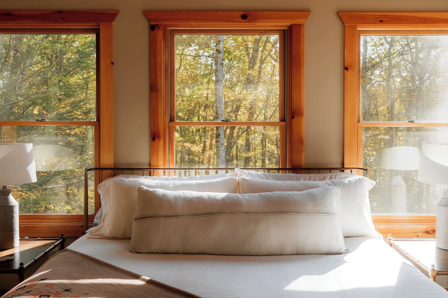 Ein Schlafzimmer mit einem Bett, zwei Nachttischlampen und großen Fenstern mit Blick auf Bäume.