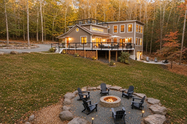 A two-story house with a deck, surrounded by a forest.