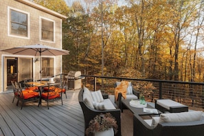 A deck with outdoor furniture, a grill, and a view of a forest.