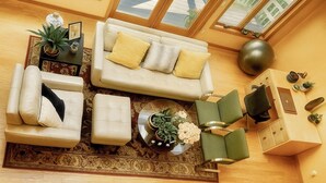 A modern living room with a sofa, ottoman, and green chairs, a coffee table with flowers, and a side table with a lamp and decorative items. - Sunny Peace Homestay (Harwinton)