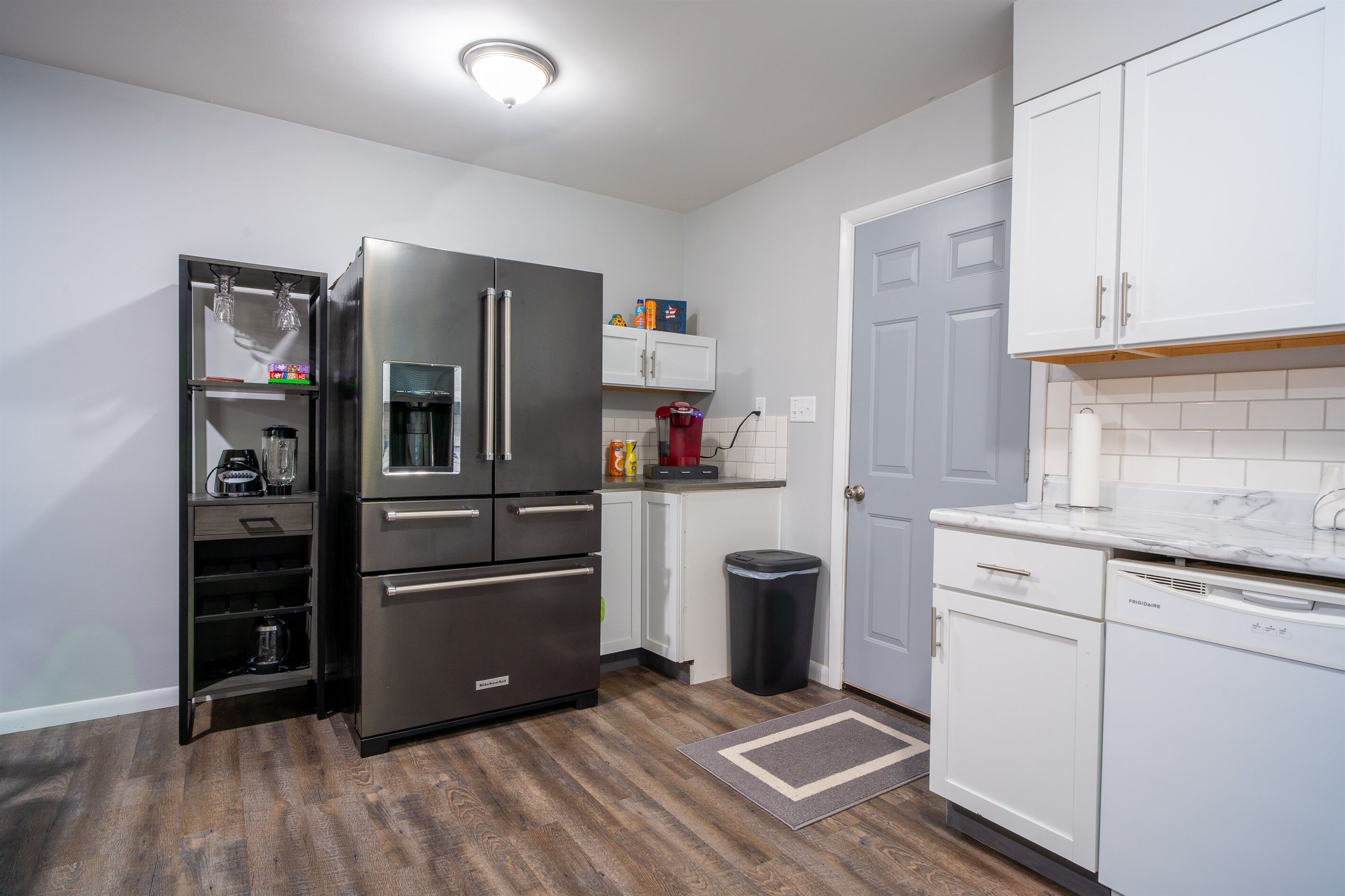 A modern kitchen with stainless steel appliances, white cabinetry, and a wooden floor.