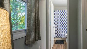 A hallway with a window, a door leading to a bathroom with patterned shower curtains, and a rug on the floor.