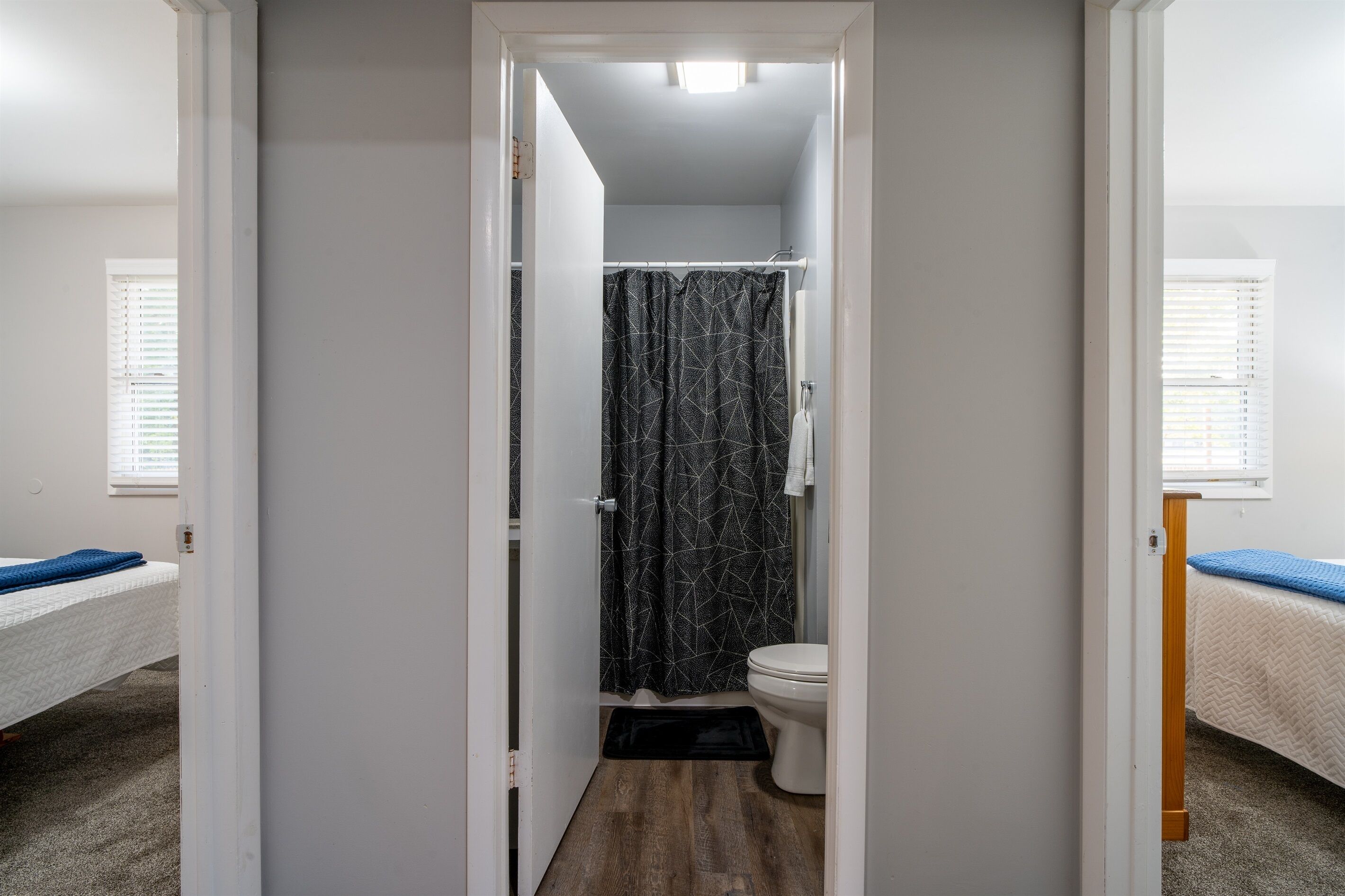 A narrow hallway leading to a bathroom with a shower curtain, a toilet, and a bed with a blue bedspread.