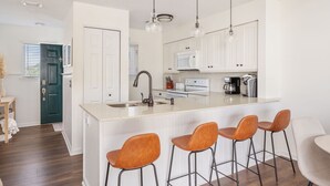 A modern kitchen with white cabinetry, a central island with bar stools, and pendant lighting.