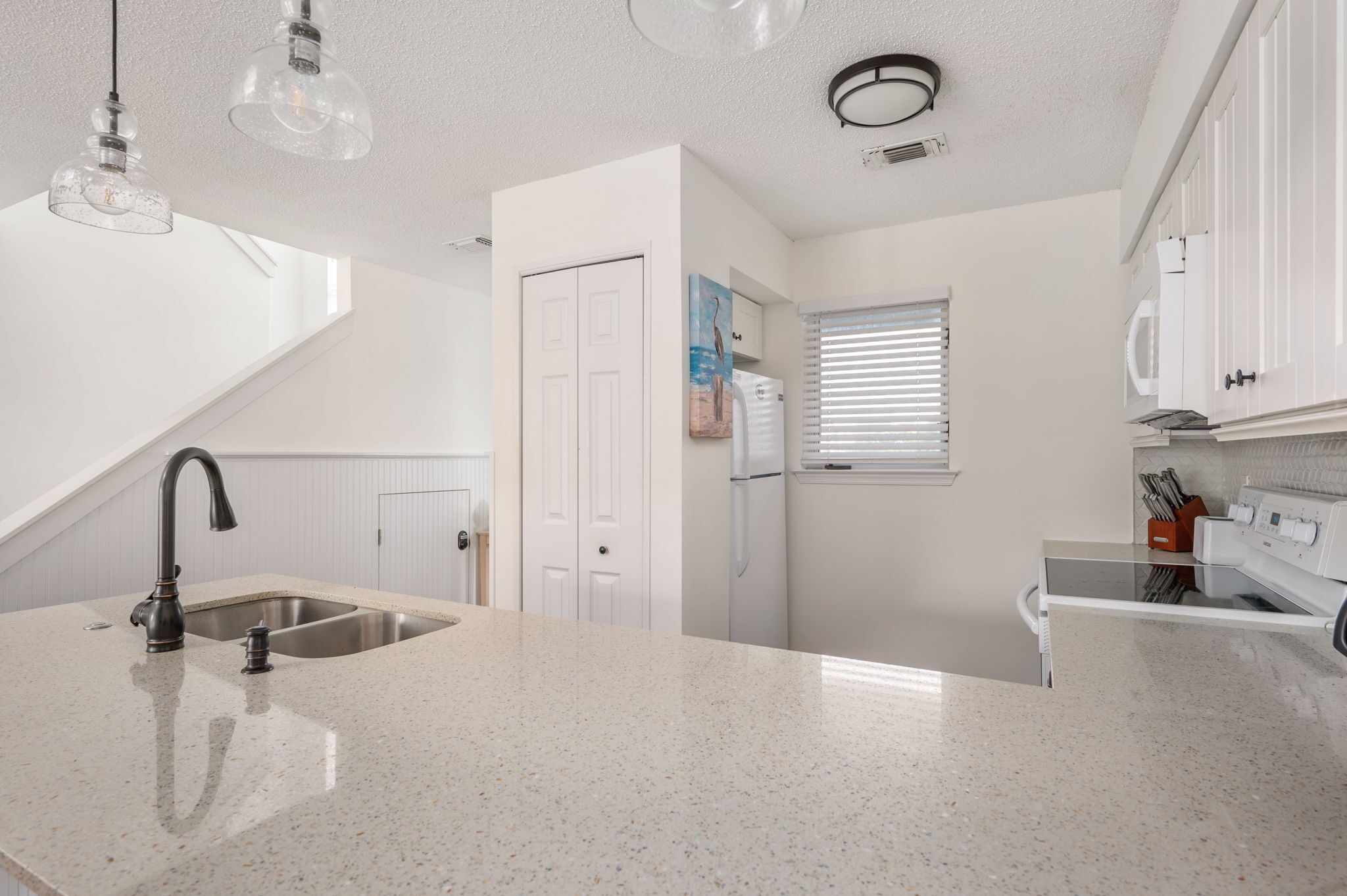A kitchen with a granite countertop, stainless steel sink, and white cabinetry.