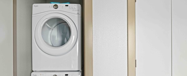 A front-loading Whirlpool washer in a laundry room with a beige wall and a white door. - Perfectly located Suite in Austin w/ full kitchen, rooftop pool, fire pit, etc! (Austin)