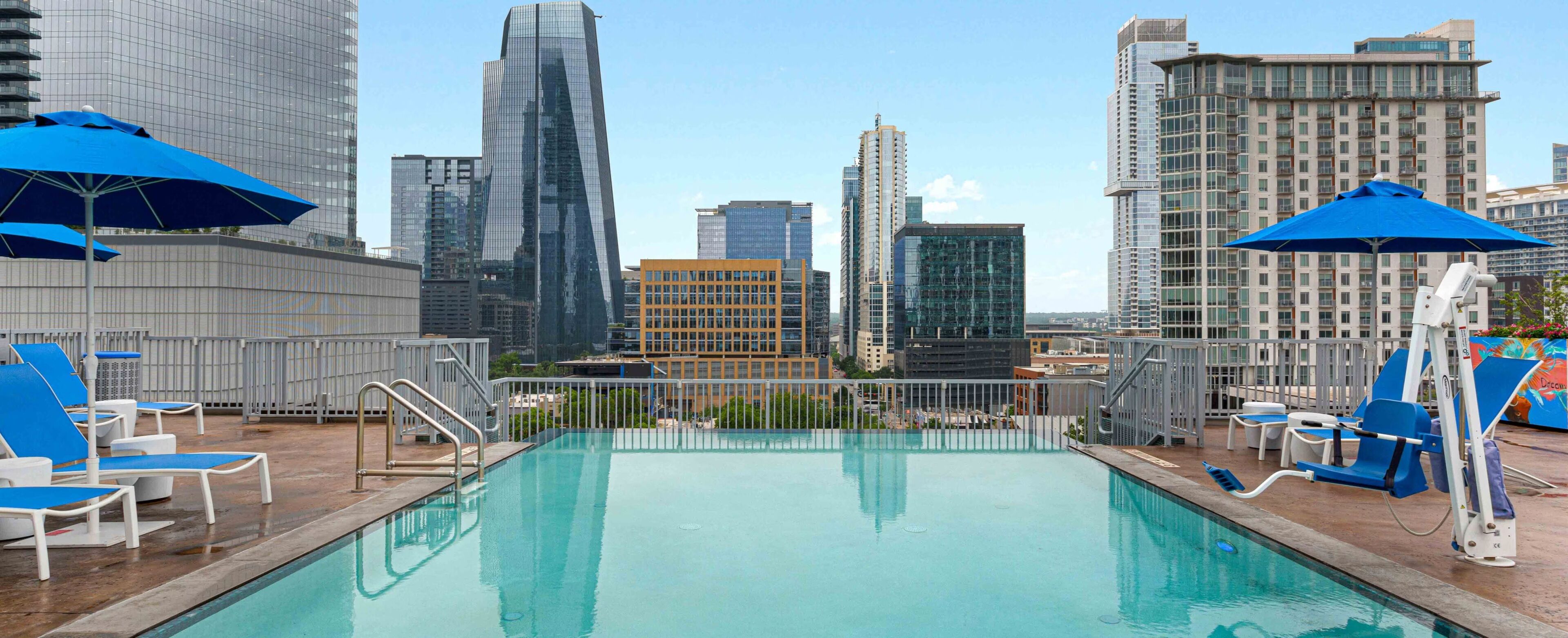 A rooftop pool with blue umbrellas, surrounded by modern high-rise buildings.