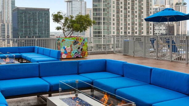 A rooftop lounge with blue seating, a glass table with a fire feature, and a colorful mural. - Perfectly located Suite in Austin w/ full kitchen, rooftop pool, fire pit, etc! (Austin)
