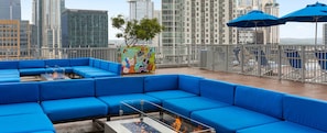 A rooftop lounge with blue seating, a glass table with a fire feature, and a colorful mural.