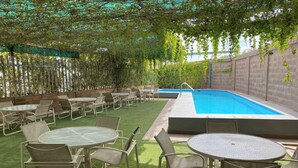 Un espace extérieur avec piscine, agrémenté de gazon synthétique, de tables et de chaises en métal, et une piscine équipée d’une échelle.