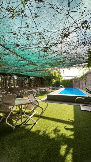 A backyard with a swimming pool, artificial grass, and outdoor furniture.