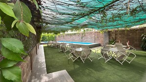 Une terrasse extérieure avec du gazon synthétique, des chaises en métal et une piscine.