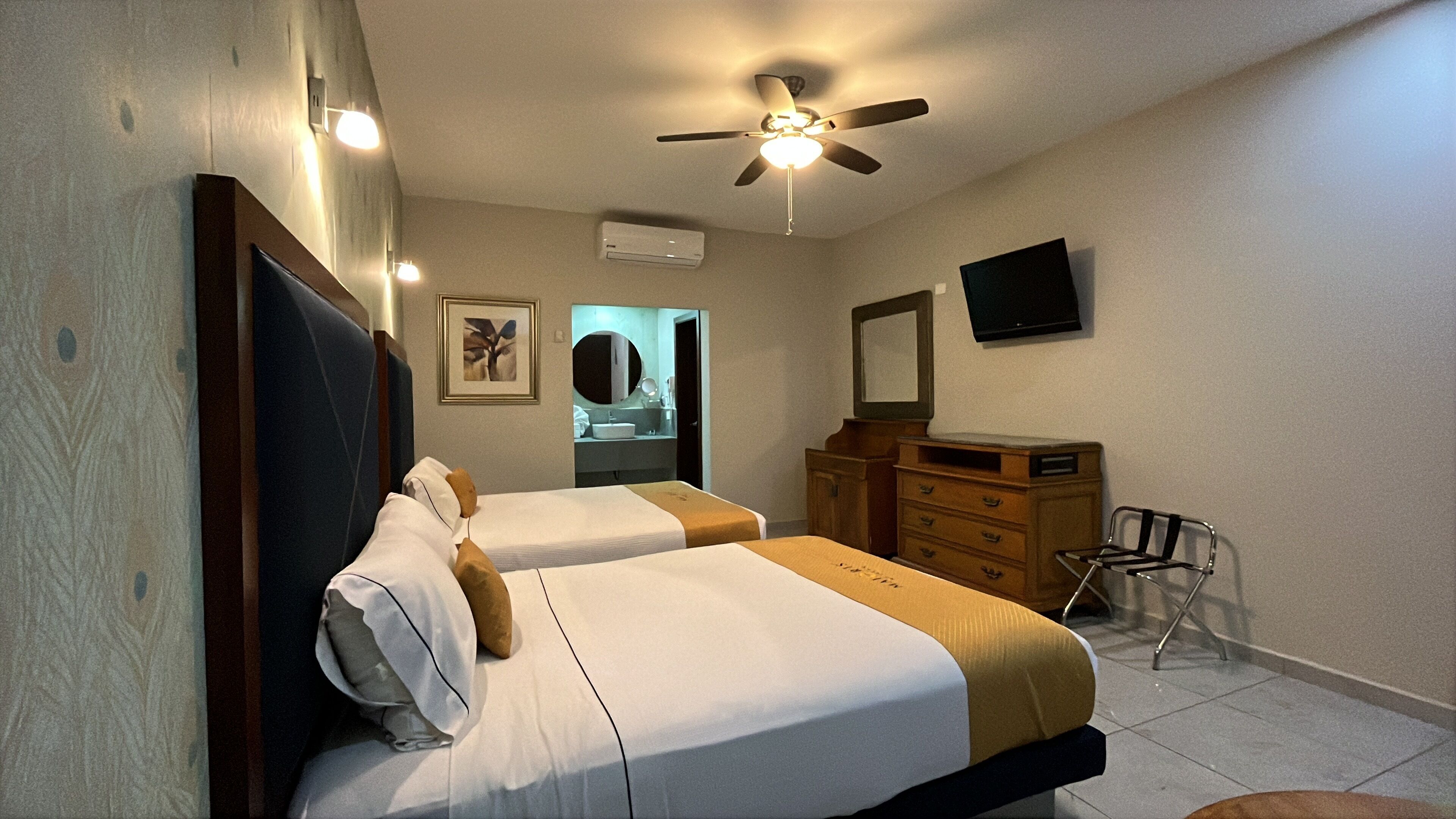 Habitación de hotel con dos camas, ventilador de techo, televisión, cómoda y una silla.