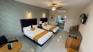 Une chambre d’hôtel avec deux lits, un ventilateur de plafond, une télévision, un bureau et une salle de bain visible au fond.