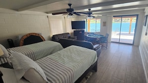 Habitación con dos camas, televisión, ventilador de techo, mesa de comedor con sillas y vista a una masa de agua a través de una puerta corrediza.