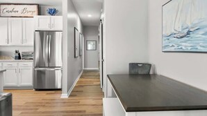 A modern kitchen with white cabinets, stainless steel appliances, and a wooden floor. - Carolina Breeze by Carolina Getaway - Spacious 3BR Condo w/ Ocean & Sound Views (Carolina Beach)