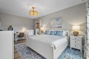 A bedroom with a bed, bedside tables, a desk, and a chair. - Carolina Breeze by Carolina Getaway - Spacious 3BR Condo w/ Ocean & Sound Views (Carolina Beach)