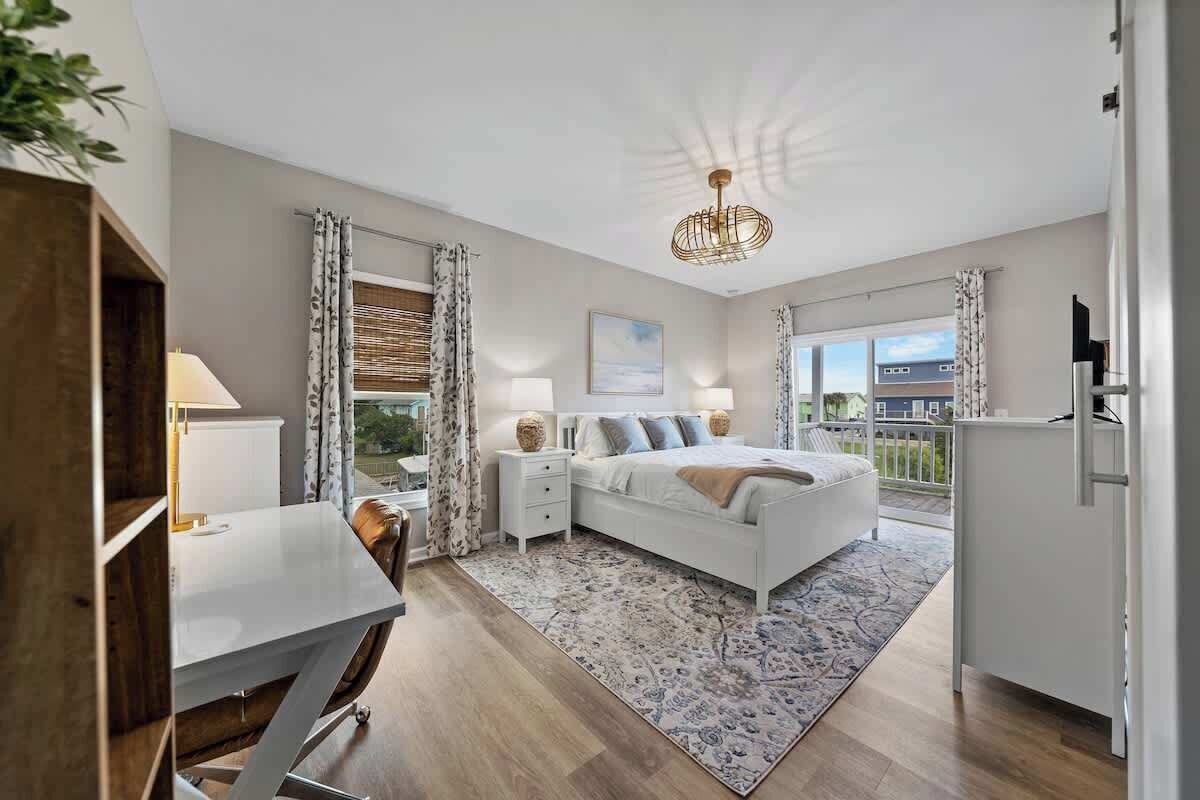 Une chambre à coucher avec un lit, des tables de chevet, un bureau et une vue sur l’extérieur.
