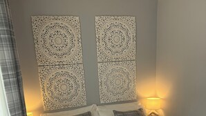 Un lit bien fait, avec une couverture à carreaux et des oreillers, deux panneaux décoratifs fixés au mur et des lampes de chevet.