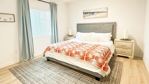 Une chambre à coucher avec un lit, une table de chevet, une commode, une fenêtre avec des rideaux et un tableau au mur.