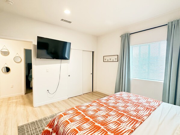 A bedroom with a bed, a TV mounted on the wall, a door, and a window with curtains.