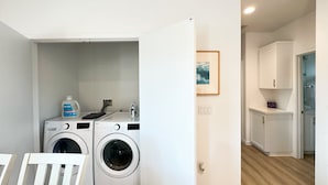 Une buanderie avec deux machines à laver blanches, une grande bouteille de lessive et une chaise blanche.